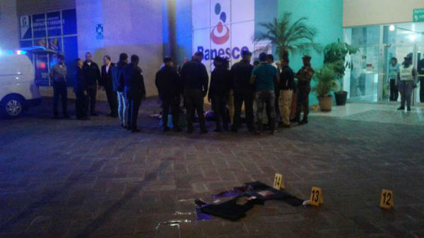 Efectivos de Policía y médicos del Inacif rodean el cadáver del custodio de valores, Manuel Vargas, muerto a tiros por dos asaltantes en la plaza Bella Vista Mall, en Santo Domingo.